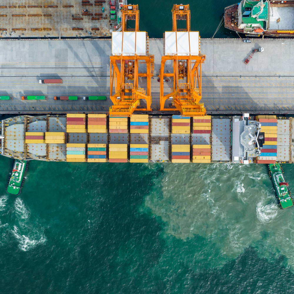 a cargo ship with cranes and boats in the water